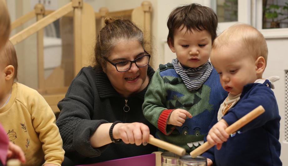 Staff teaching a baby to hit the drums.