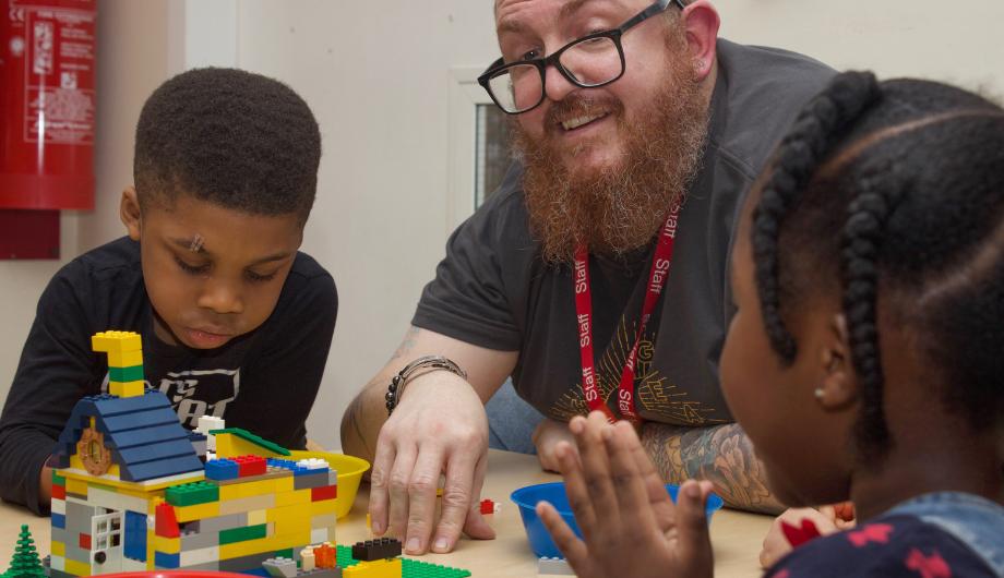 Male staff and children building a house using legos