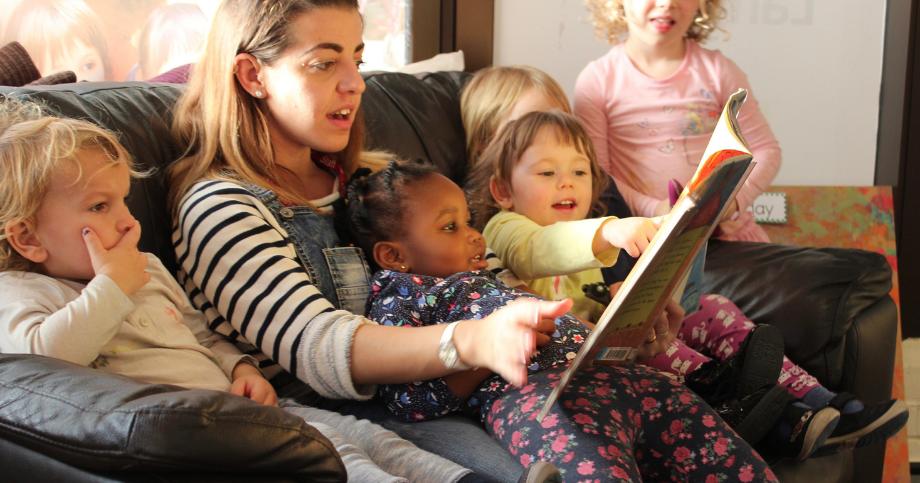 Children and staff sitting very cosy on the sofa reading a book