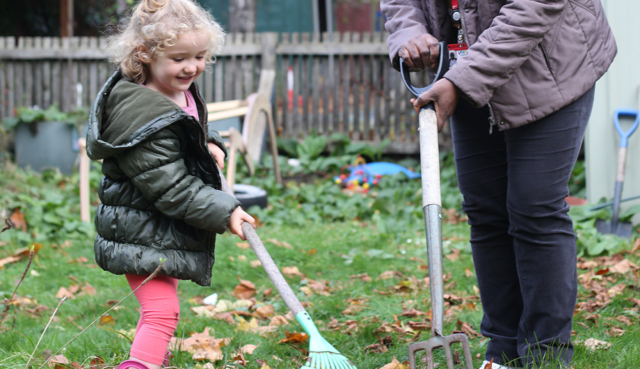 Girl raking leaves in the garden with a teacher